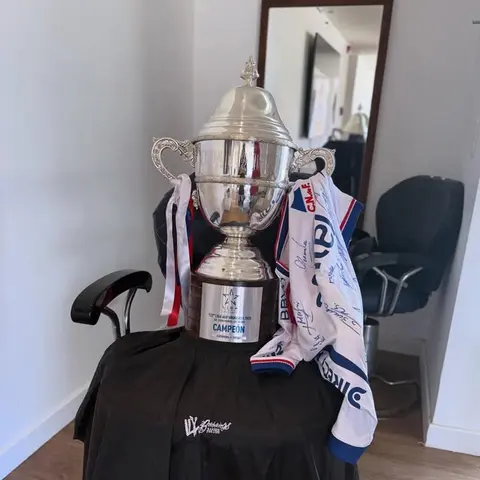 Trofeo de campeón y camiseta firmada sobre un sillón de la barbería